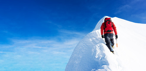 Bergbeklimmer arriveert op de top van een besneeuwde top. Begrippen: vastberadenheid, moed, inspanning, zelfrealisatie. Heldere hemel, zonnige dag, winterseizoen. Grote kopie-ruimte aan de linkerkant. Europese Alpen, Europa.