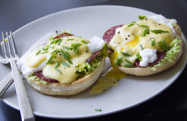 Eggs Benedict dish consisting of poached eggs and sliced ham on toasted English muffins, covered with hollandaise sauce against a dark background.
