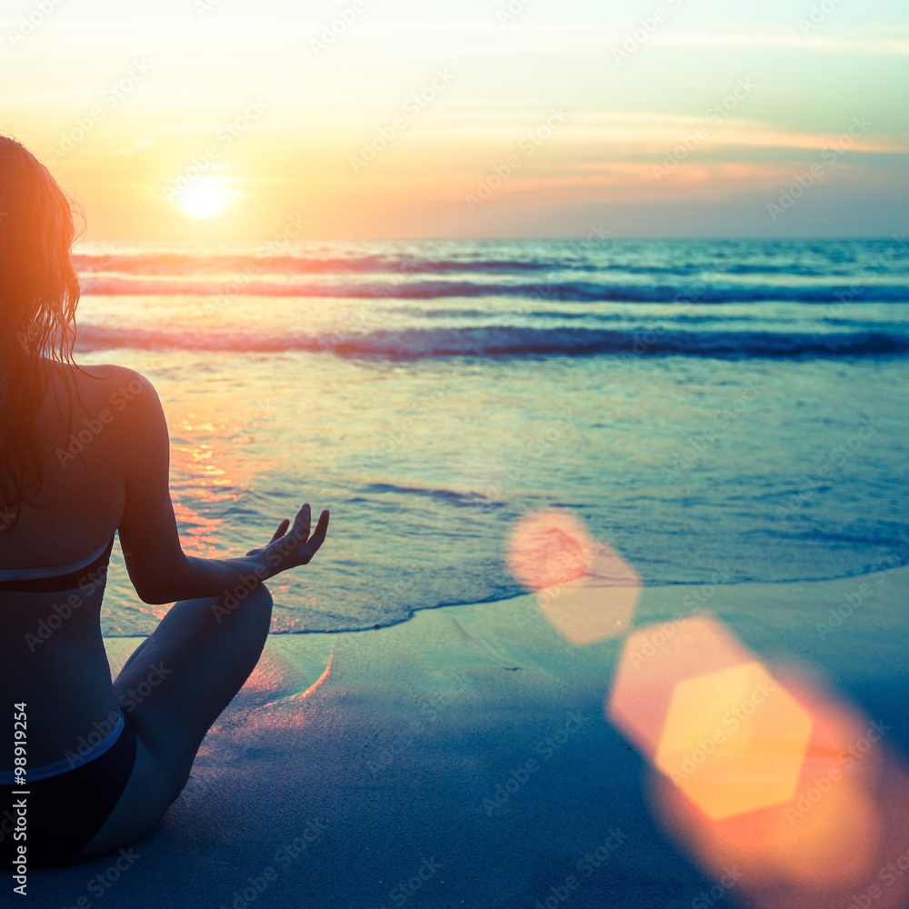 Wall mural caucasian woman practicing yoga at seashore during sunset.