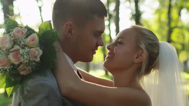 Young bride and groom are kissing in a sunny park. Shot on RED Cinema Camera.