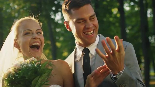 Happy bride and groom laugh and are surprised by confetti in a sunny park. Shot on RED Cinema Camera.