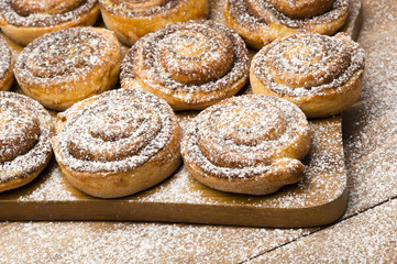 Cinnamon buns on the wooden board on the wooden background.