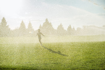 Little boy running on the green field in the rain