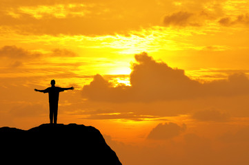 Silhouette of a man open hands on top of mountain during sunset