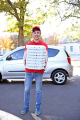 Pizza delivery boy holding boxes with pizza near car