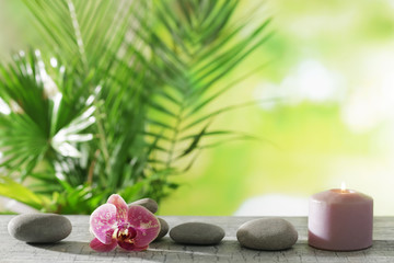 Spa composition of candle, stones and orchid on blurred background