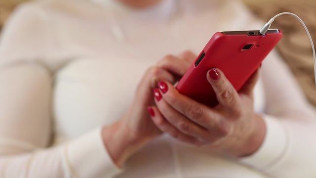 Close up of woman hands with red smartphone. Woman looks and flips through the photos in her smartphone. Female with smartphone. Businesswoman with red mobile phone with earphones