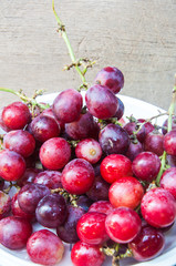 Red grape berries in white plate on wood