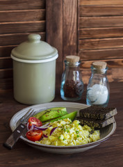 Healthy breakfast or snack - eggs scramble, avocado and cherry tomatoes on a brown wooden surface
