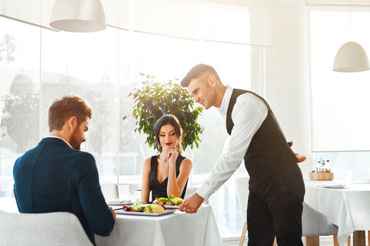 Happy Couple In Love Having Romantic Dinner In Luxury Gourmet Restaurant. Waiter Serving Meal. People Celebrating Anniversary Or Valentine's Day. Romance, Relationship Concept. Healthy Food Eating.