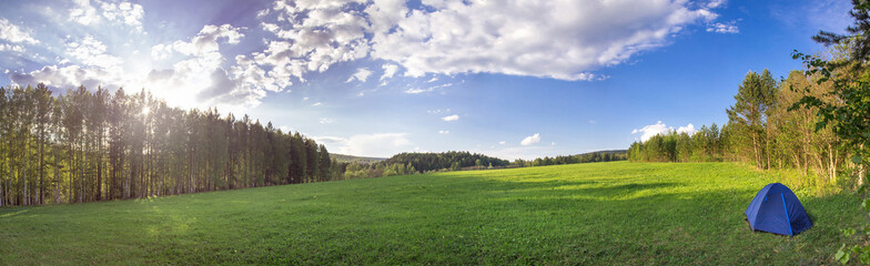 Fototapeta na wymiar Panorama of the lush green spring meadows, tent and trees