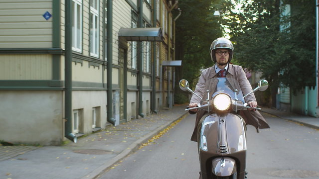 Young man in an elegant beige trench coat rides a retro scooter in a rural residential area. Shot on RED Cinema Camera.