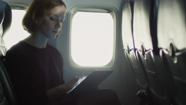 Young woman is using a tablet inside an airplane next to a window. Shot on RED Cinema Camera.