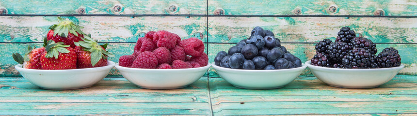 Blackberry, strawberry, blueberry and blackberry in white bowl over wooden background