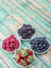 Blackberry, strawberry, blueberry and blackberry in white bowl over wooden background