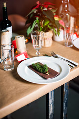 Decorated Christmas holiday table ready for dinner. Beautifully decorated table set with candles, spruce twigs, plates and serviettes for event in the restaurant.