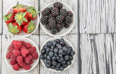 Blackberry, strawberry, blueberry and blackberry in white bowl over wooden background