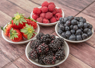 Blackberry, strawberry, blueberry and blackberry in white bowl over wooden background