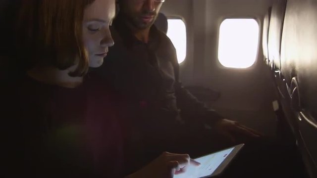 Couple are sitting together on a plane and using tablet. Shot on RED Cinema Camera.