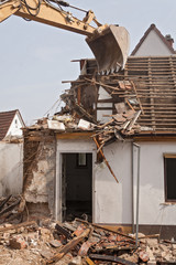 A large track hoe excavator tearing down an old house