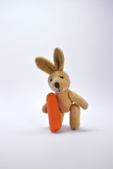 Little brown Plush Rabbit posing in a white background with a carrot and looking at the camera