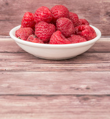 Raspberry fruit in white bowl over wooden background