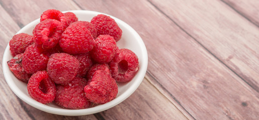 Raspberry fruit in white bowl over wooden background