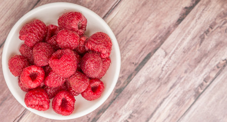 Raspberry fruit in white bowl over wooden background