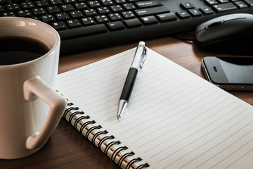 Pen on notebook with computer keyboard, mouse and cell phone