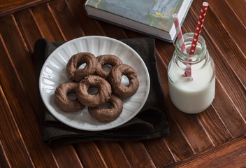 Healthy chocolate cookies, bottle of milk and a book on a brown wooden surface. A delicious breakfast or snack