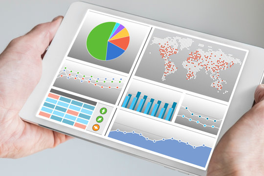 Hand holding modern tablet or mobile device with analytics dashboard for sales, marketing, accounting, controlling department to check revenue, sales and business KPIs