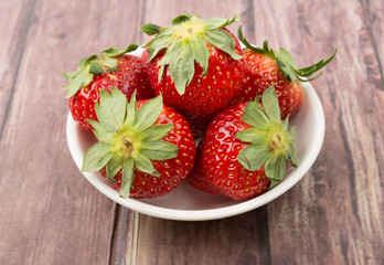 Strawberry fruits in white bowl over wooden background