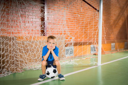 Glum young boy sitting waiting in the goalposts - Powered by Adobe