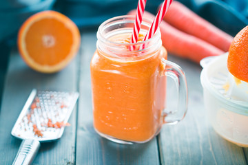 Healthy carrot orange smoothie in a jar with tube wooden background. 