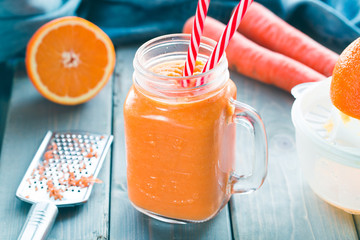 Healthy carrot orange smoothie in a jar with tube wooden background. 