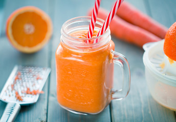 Healthy carrot orange smoothie in a jar with tube wooden background. 