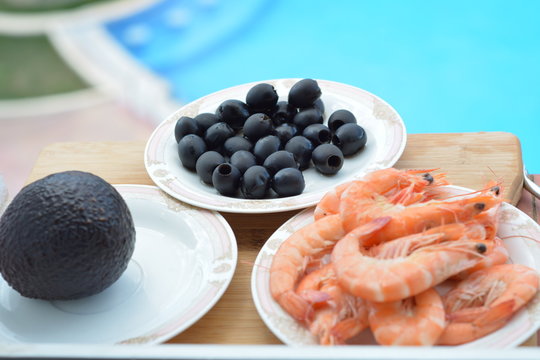 do olives and shrimp on separate plates on the table next to the swimming pool.

