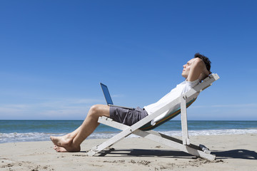Successful businessman resting on a tropical beach with laptop
