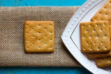 Square cracker biscuits on a linen napkin and a triangular portion of white ceramic plates with...