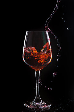 Red wine pouring into  wine glass. Isolated on black background