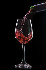 Red wine pouring into  wine glass. Isolated on black background