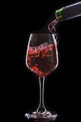 Red wine pouring into  wine glass. Isolated on black background
