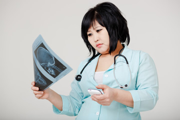 Young female Asian doctor with cell phone looking at the x-ray p