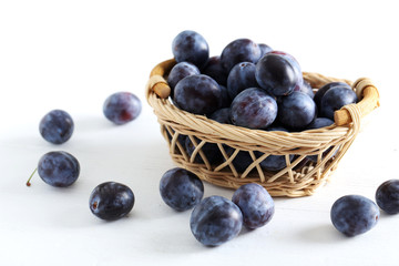 Fresh plums in basket on the white wooden background