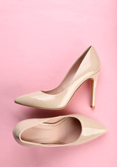 Pair of beige women's high-heeled shoes on pink background