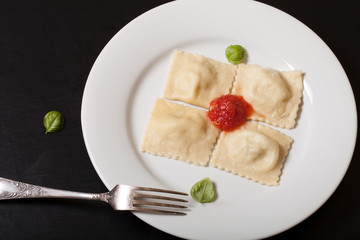 Russian ravioli - pelmeni with tomato sauce and basil on a white