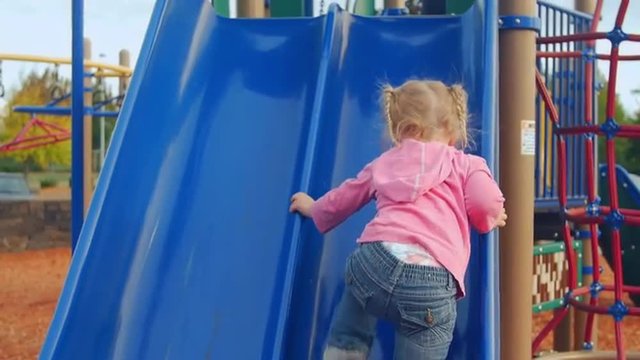 Cute little girl tries her best to climb up the slide at the park