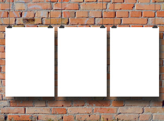 Close-up of three hanged paper sheet frames with clips on brick wall background