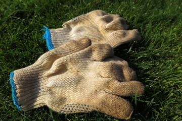 Dirty and worn-out gardening textile gloves on the mown lawn after hard work in the autumn garden