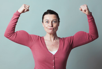 muscle concept - smiling 40s woman lifting her muscles up for metaphor of female independence and...